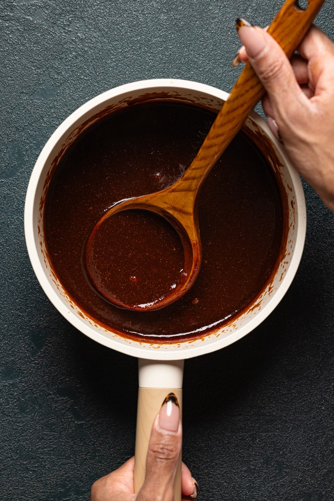 Sauce in a saucepan being held with a wooden spoon.