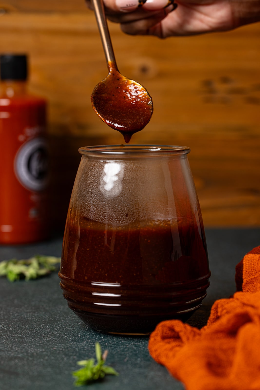 BBQ sauce in a mason jar with a spoon being held.