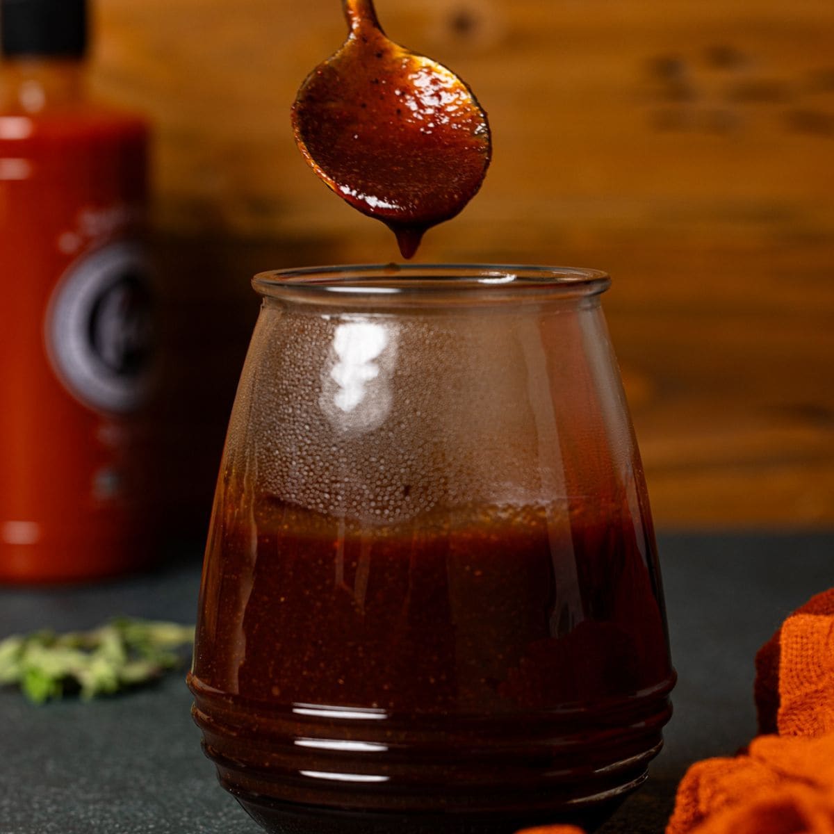 BBQ sauce in a mason jar with a spoon being held.