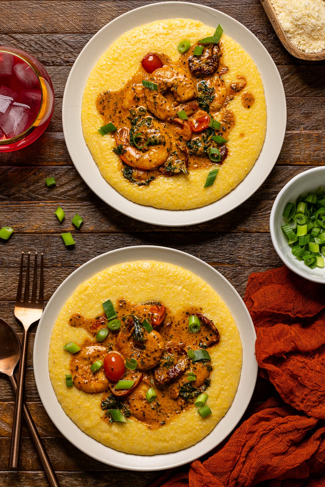 Two plates of shrimp and grits with two forks and a drink.