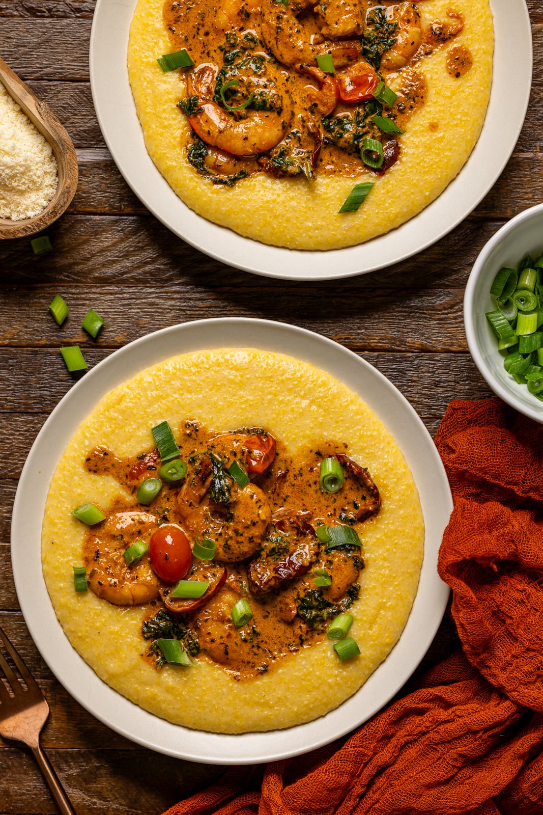 Shrimp and grits in two plates with a side of scallion and parmesan.