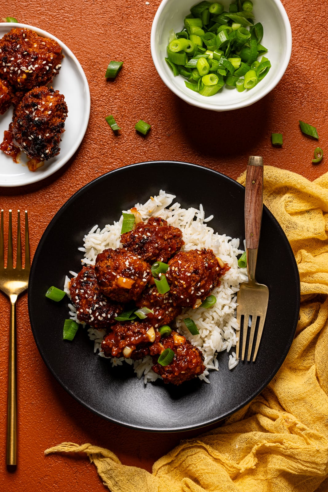 General Tso Chicken in a black plate with a fork and a bowl of chopped green onions.