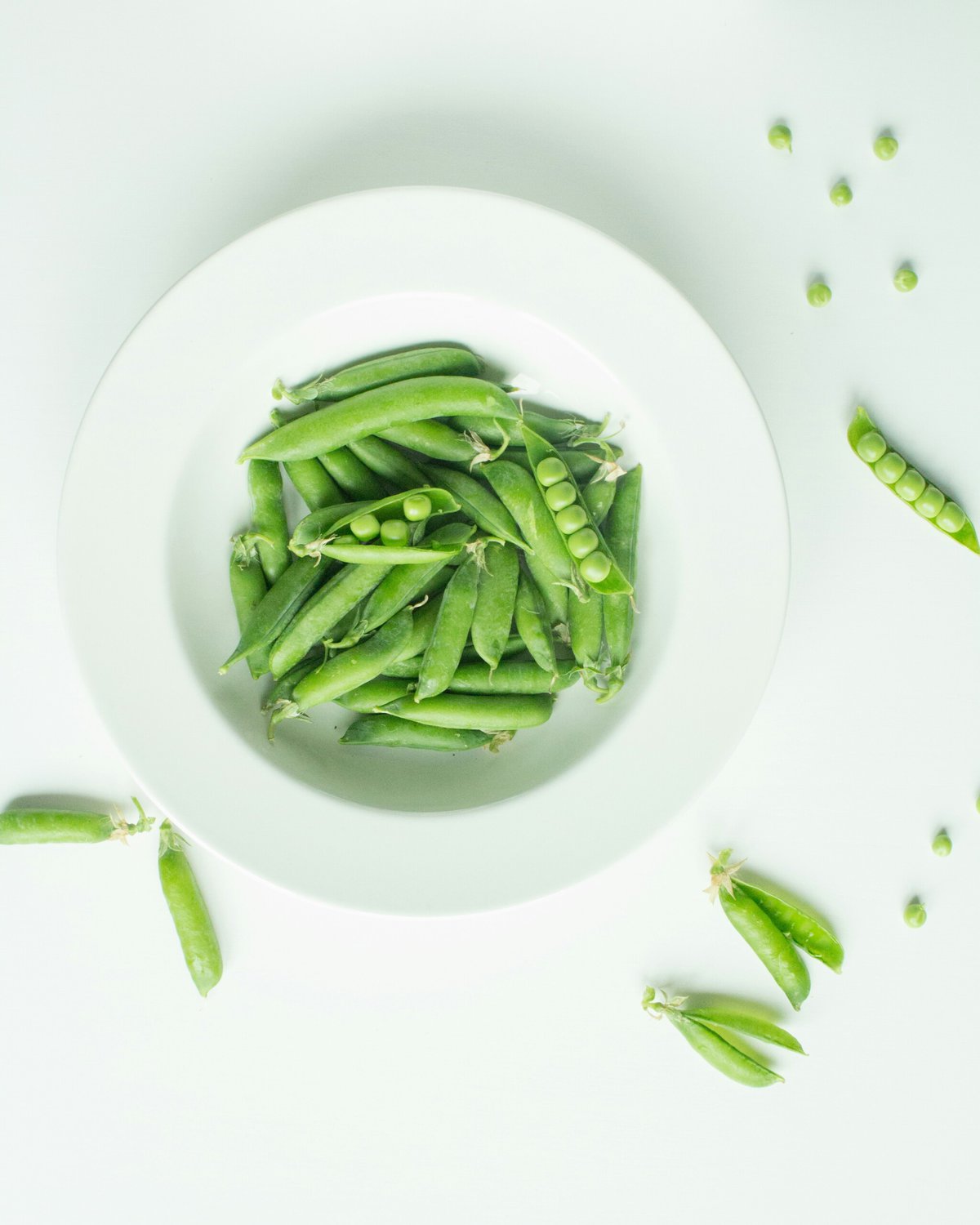 Vegan source of protein green peas in shell in a white bowl.