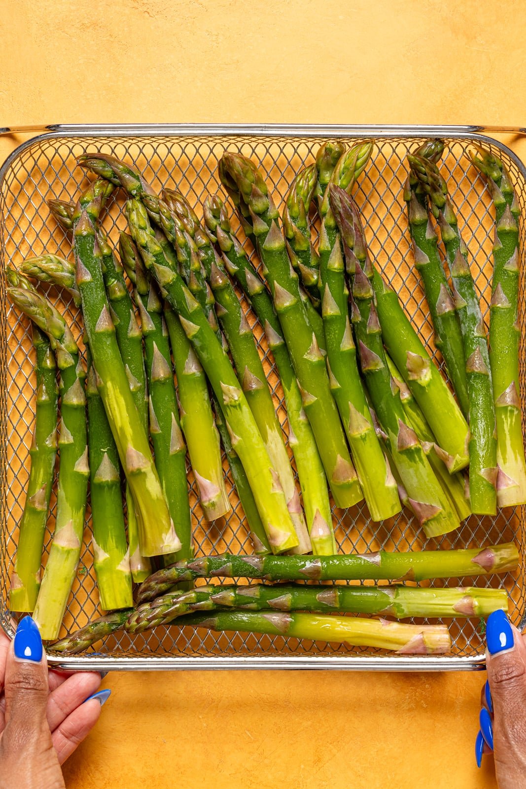 Asparagus in an Air Fryer basket being held.