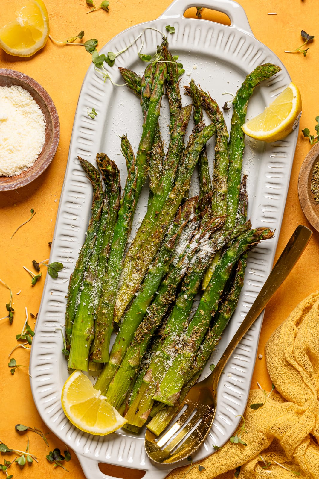 Asparagus on a platter with parmesan cheese and lemons.
