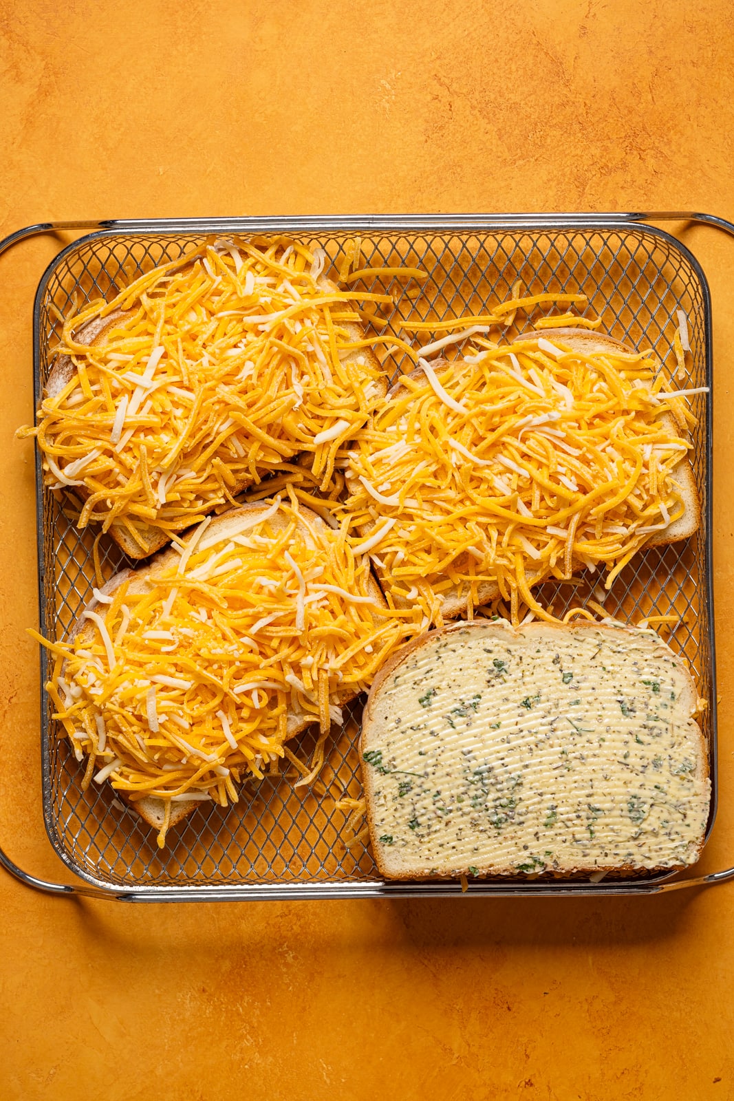 Shredded cheese on slices of bread with herb butter in an Air Fryer basket.