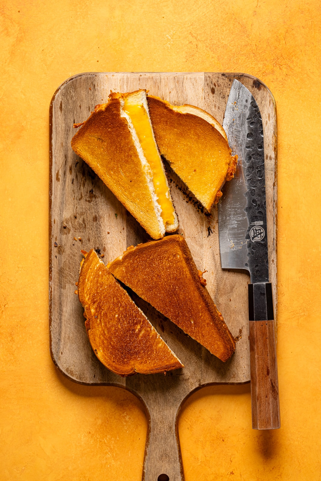 Sliced grilled cheeses on a cutting board with a knife.