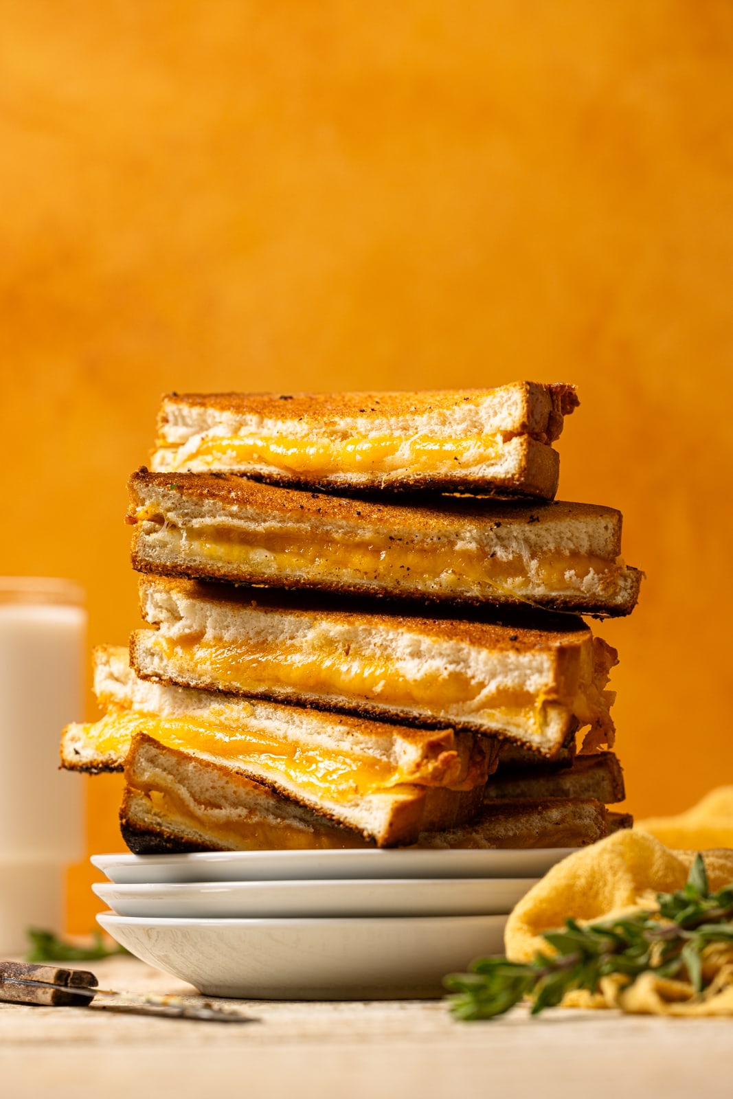 Stack of grilled cheese sandwiches on white plates with a glass of milk.
