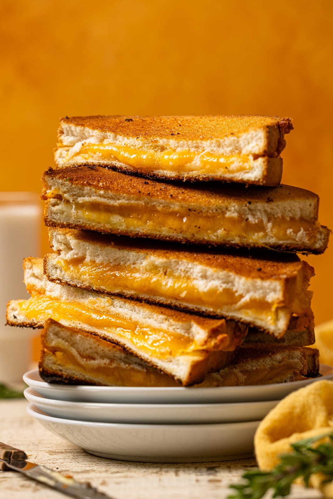 Stack on grilled cheese on white plates with an orange background.
