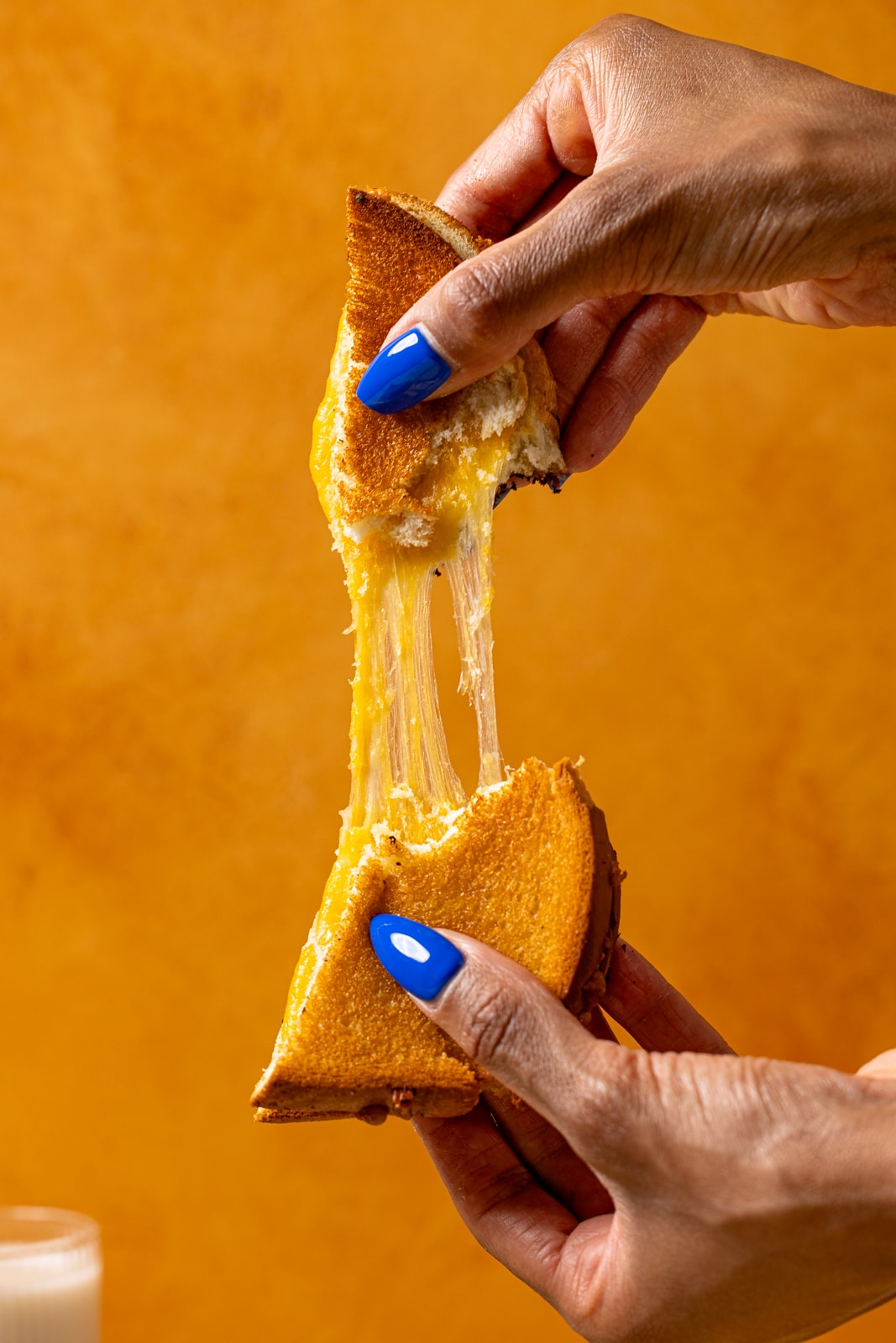 Grilled cheese being pulled apart held in hand.