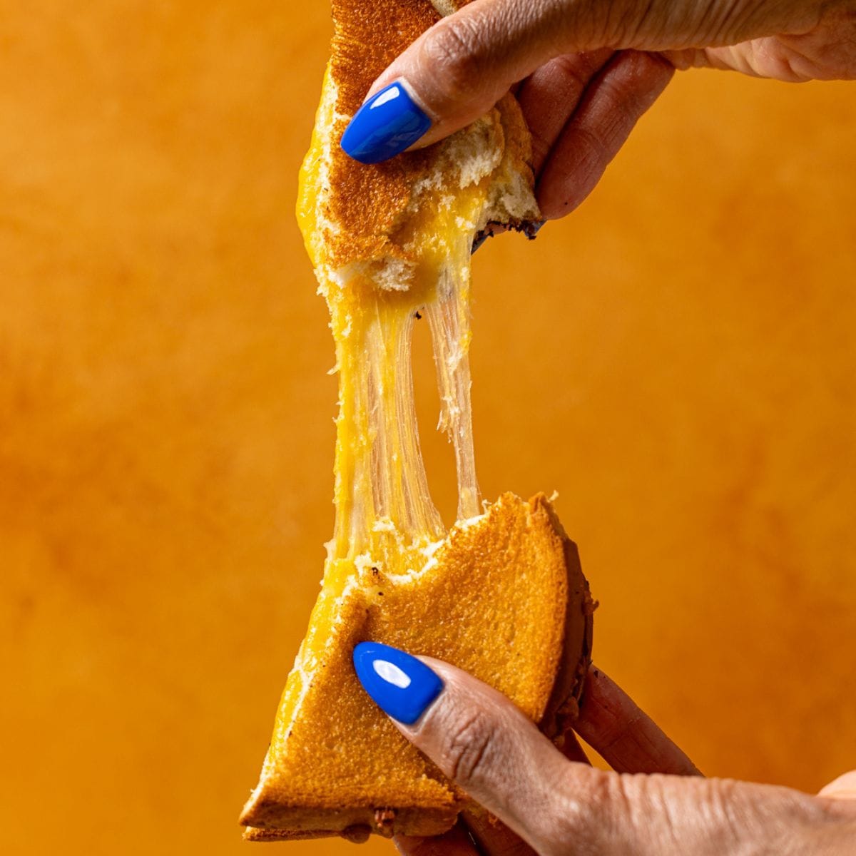 Grilled cheese being pulled apart held in hand.