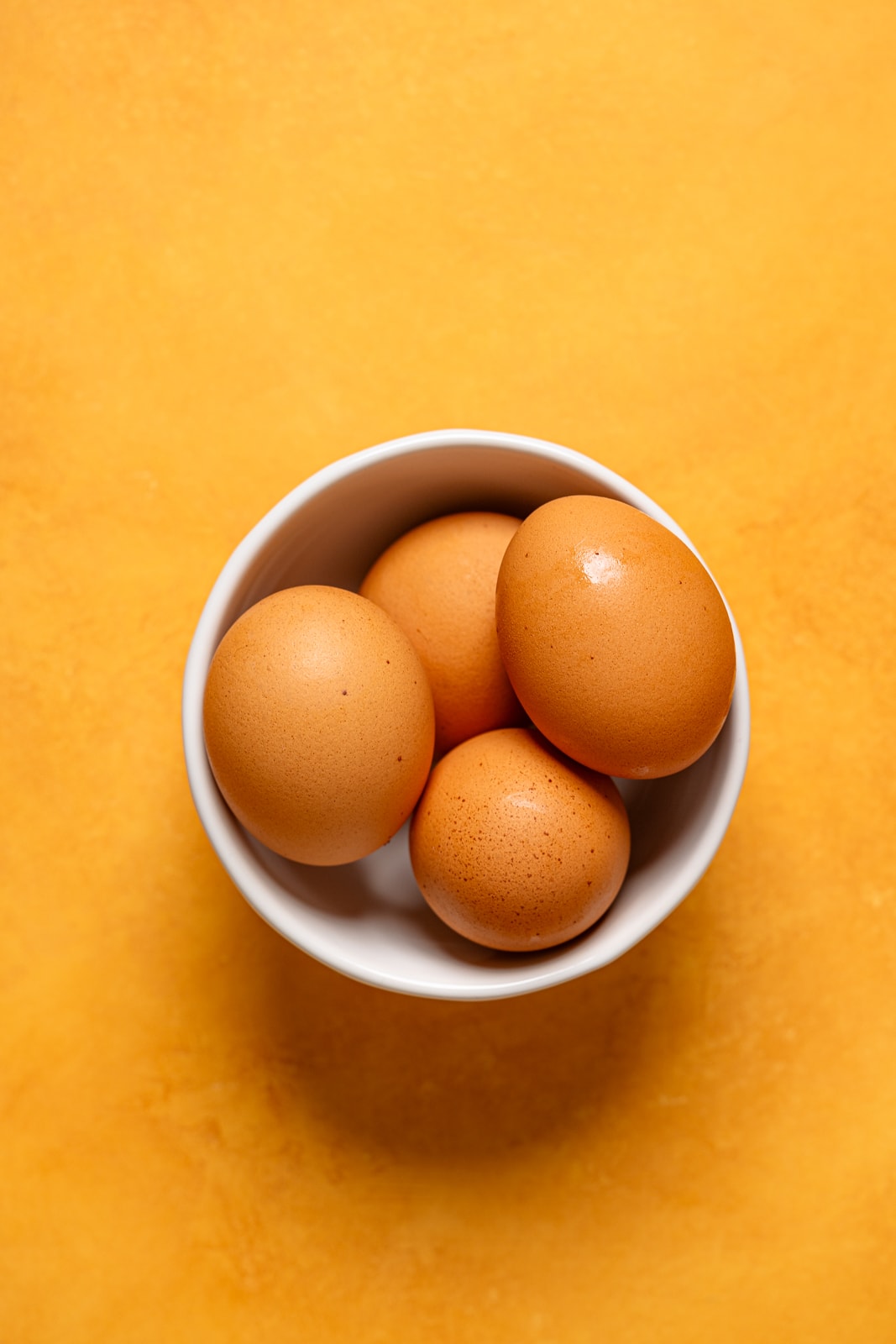 Eggs in a bowl on an orange table.