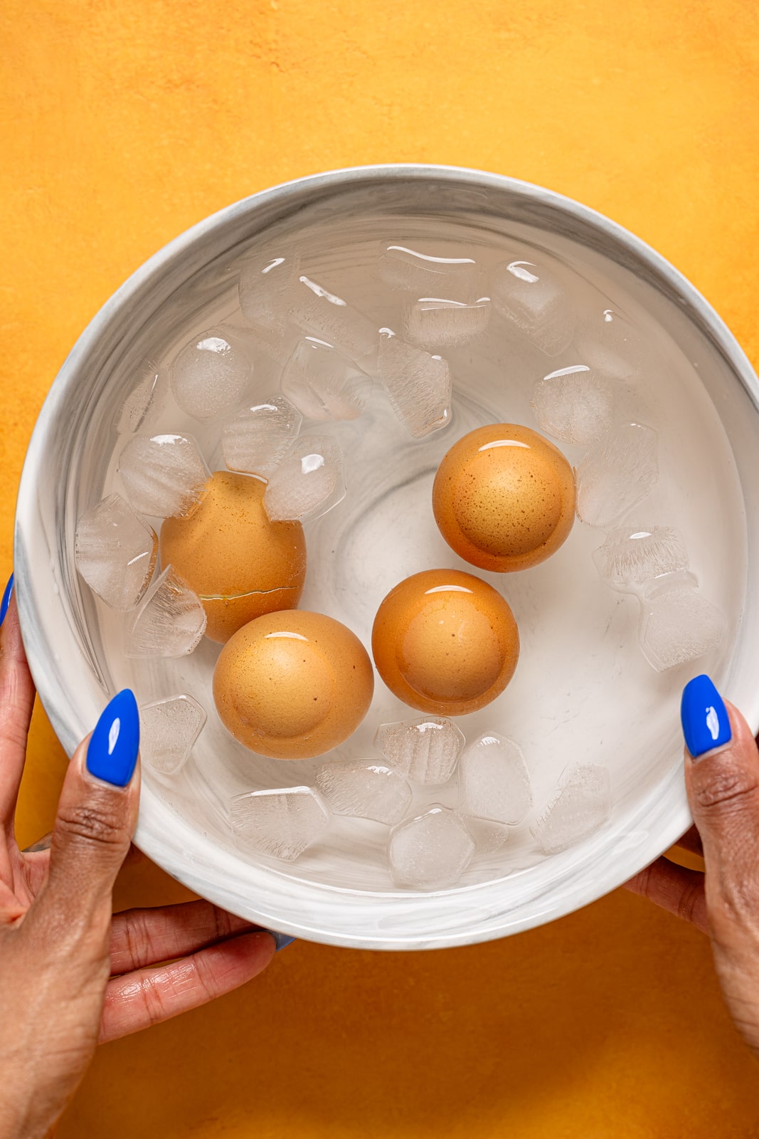 Cooked boiled eggs in a cold water bowl being held.