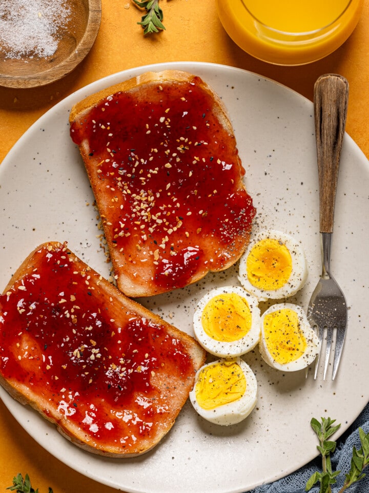 Eggs with jam toast on a plate with a fork and drink.