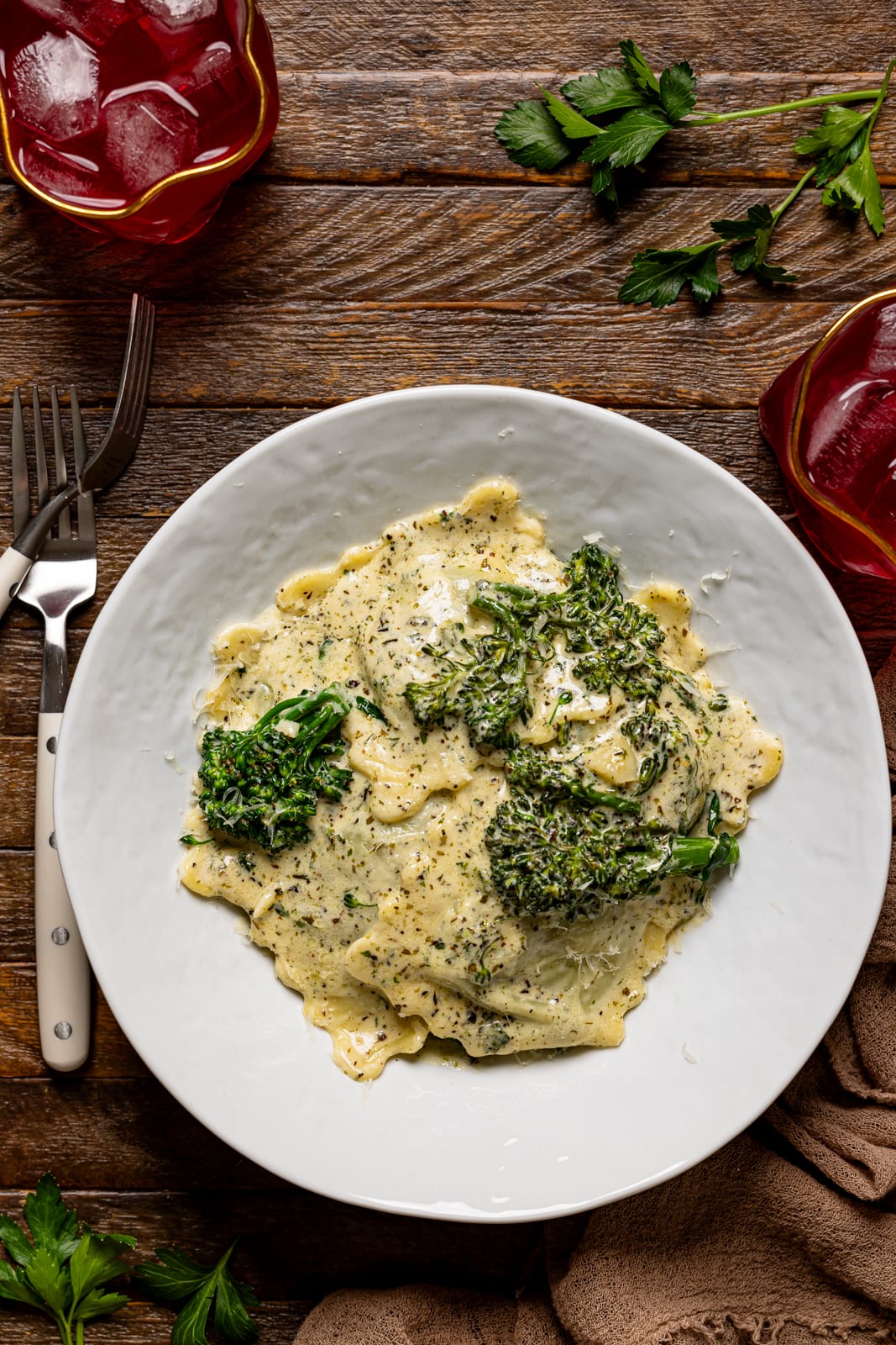 Ravioli in a white plate with two forks and two drinks.