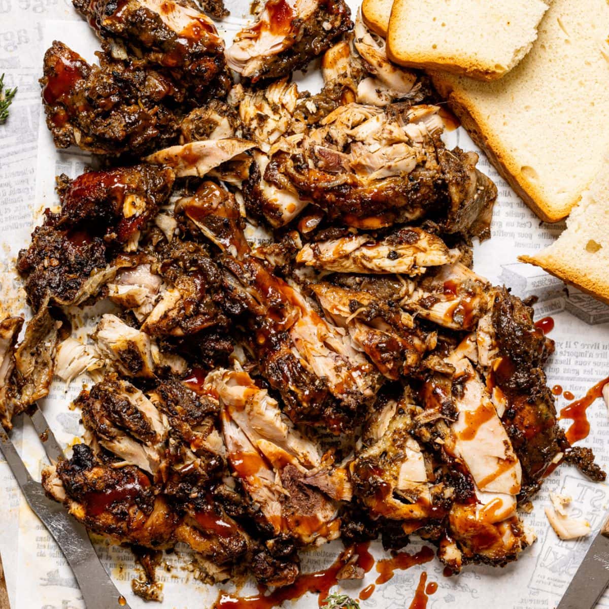 Chopped jerk chicken on a cutting board with BBQ sauce, bread, and a fork.