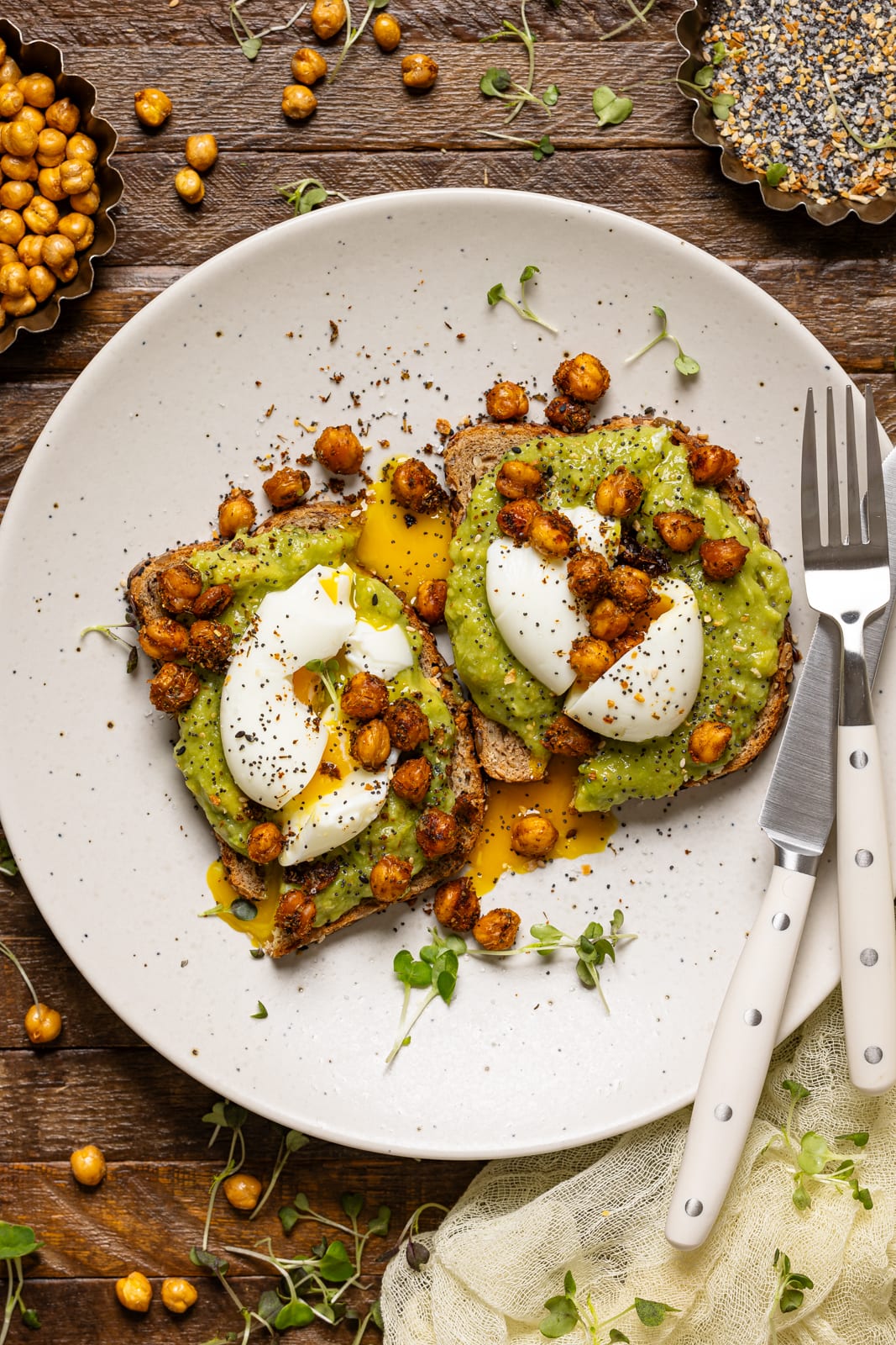 Avocado toast on a white plate with a fork and side of roasted chickpeas.