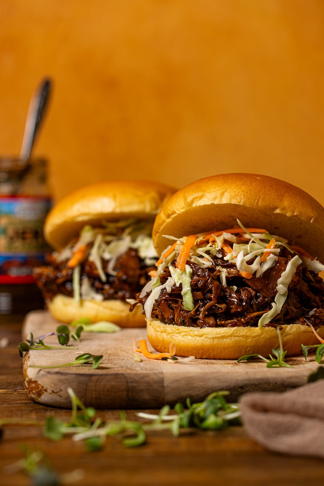 Two pulled pork sandwiches on a cutting board with jerk sauce in the background.