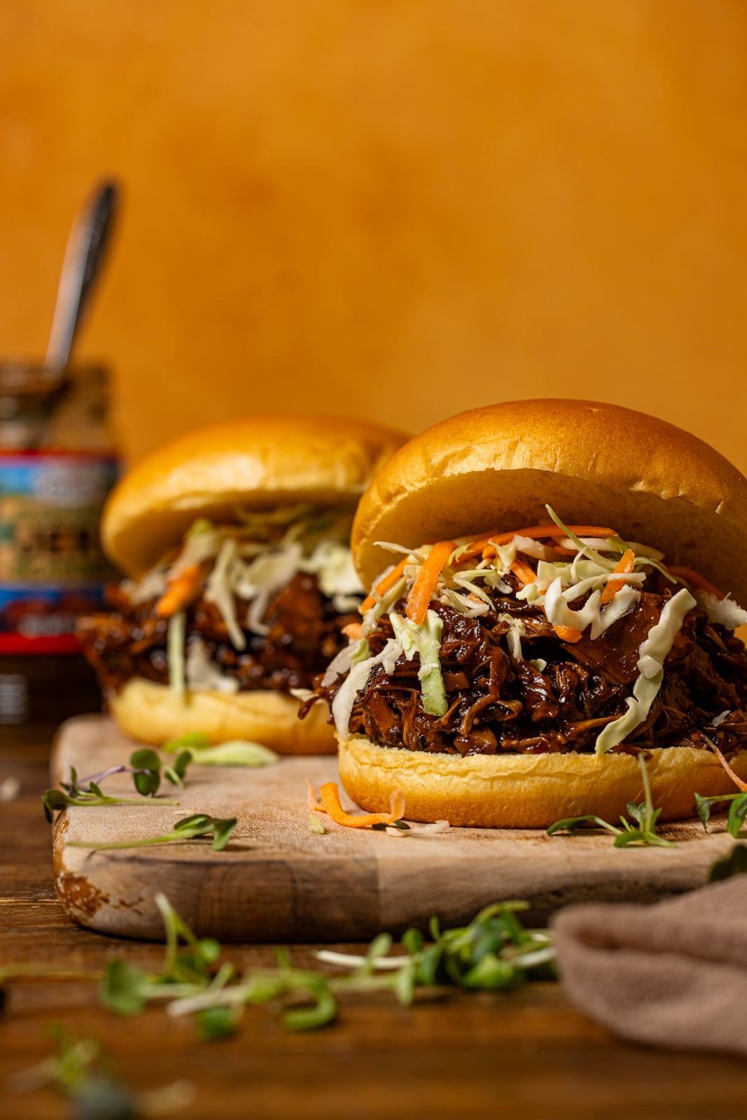 Two pulled pork sandwiches on a cutting board with jerk sauce in the background.