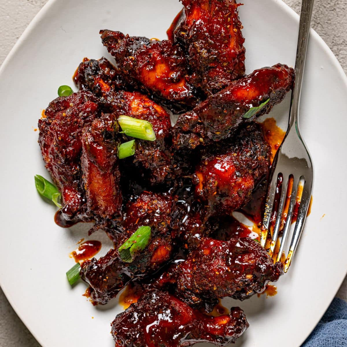 Up close shot of Honey BBQ Chicken wings on a white plate with a fork.