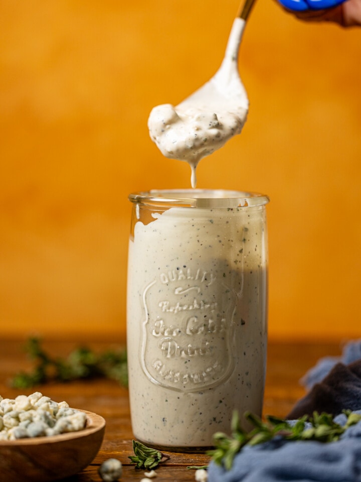 Blue cheese dressing in a mason jar being held by a spoon.