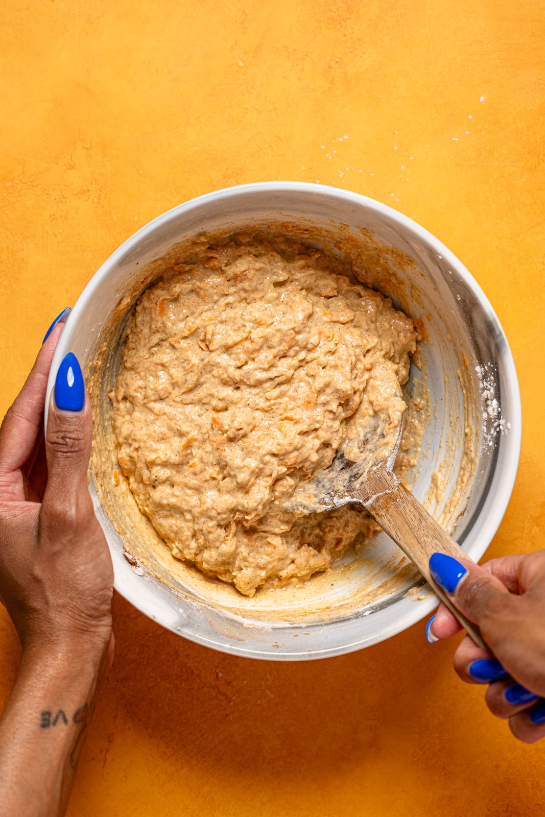 Batter in a bowl being mixed with a wooden spoon.