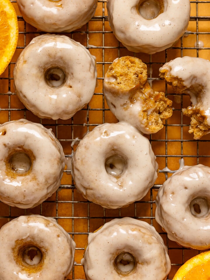 Up close donuts on a wire rack with oranges.