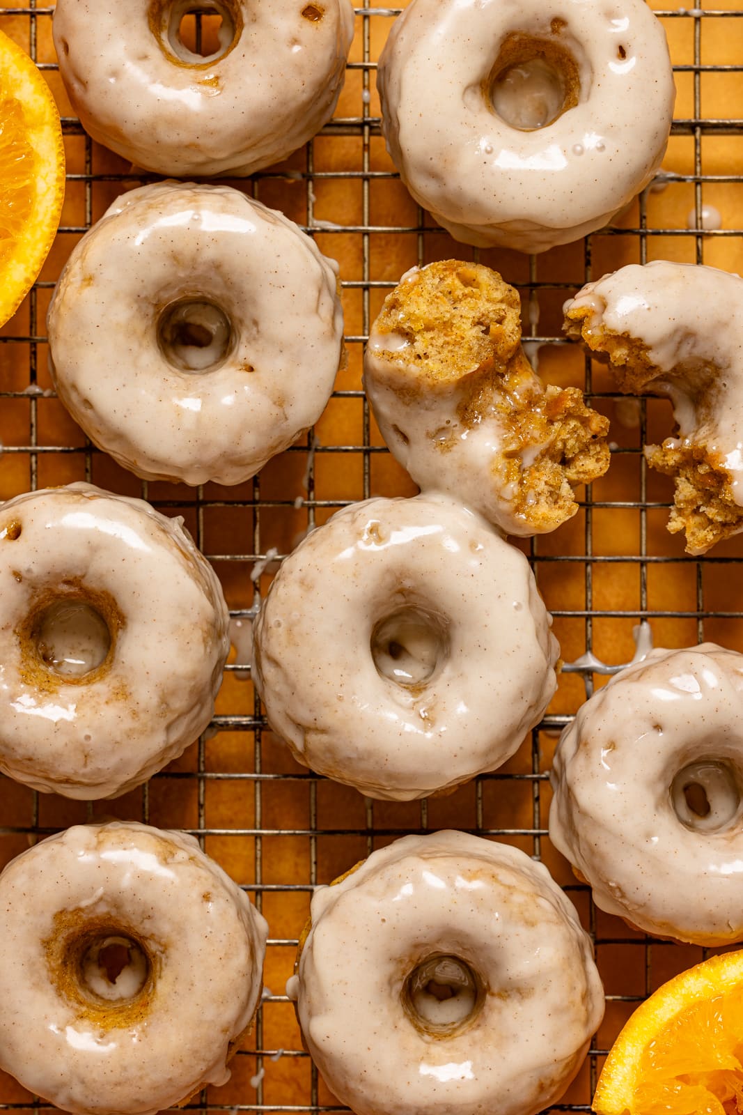 Up close donuts on a wire rack with oranges.