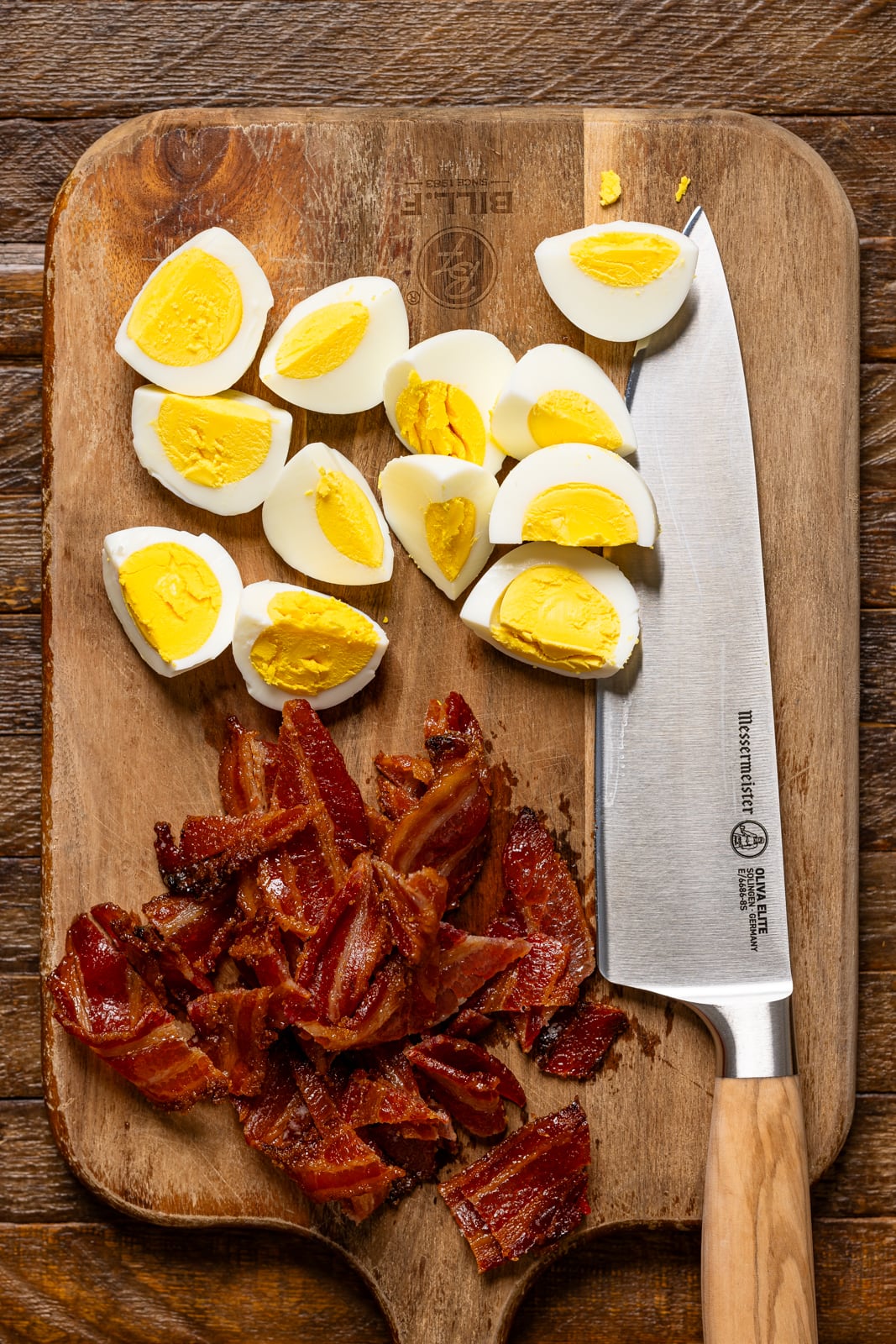 Chopped eggs and bacon on a cutting board with a knife. 