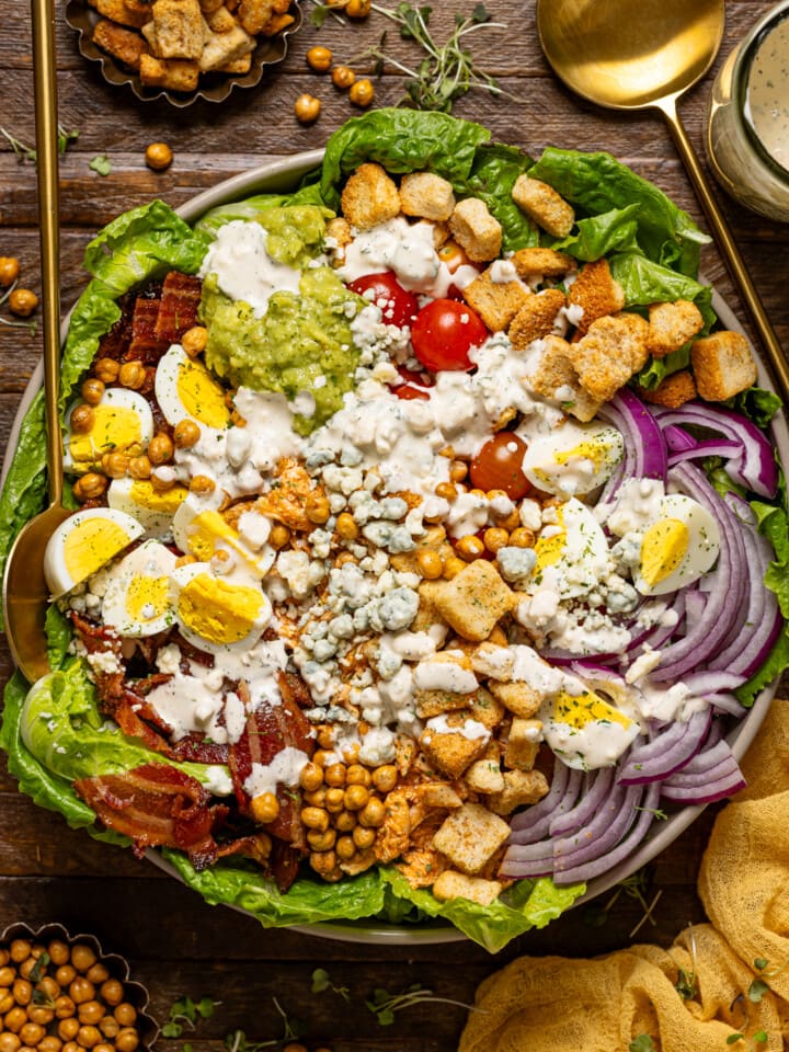 Cobb salad in a bowl with serving spoons.