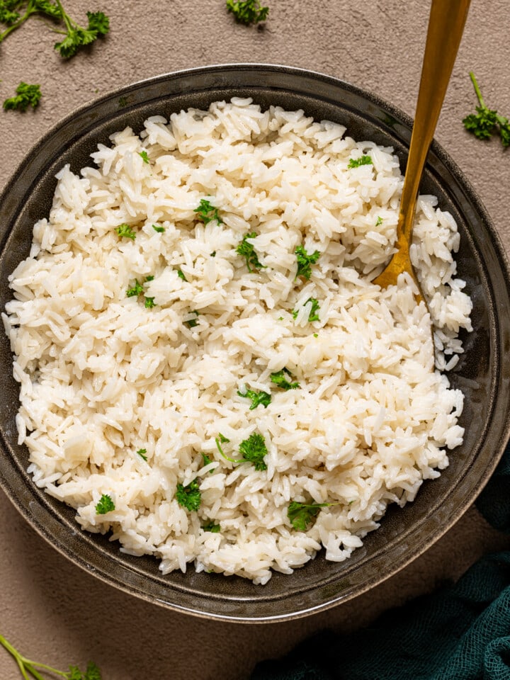 Rice in a black bowl on a grey table with a spoon.