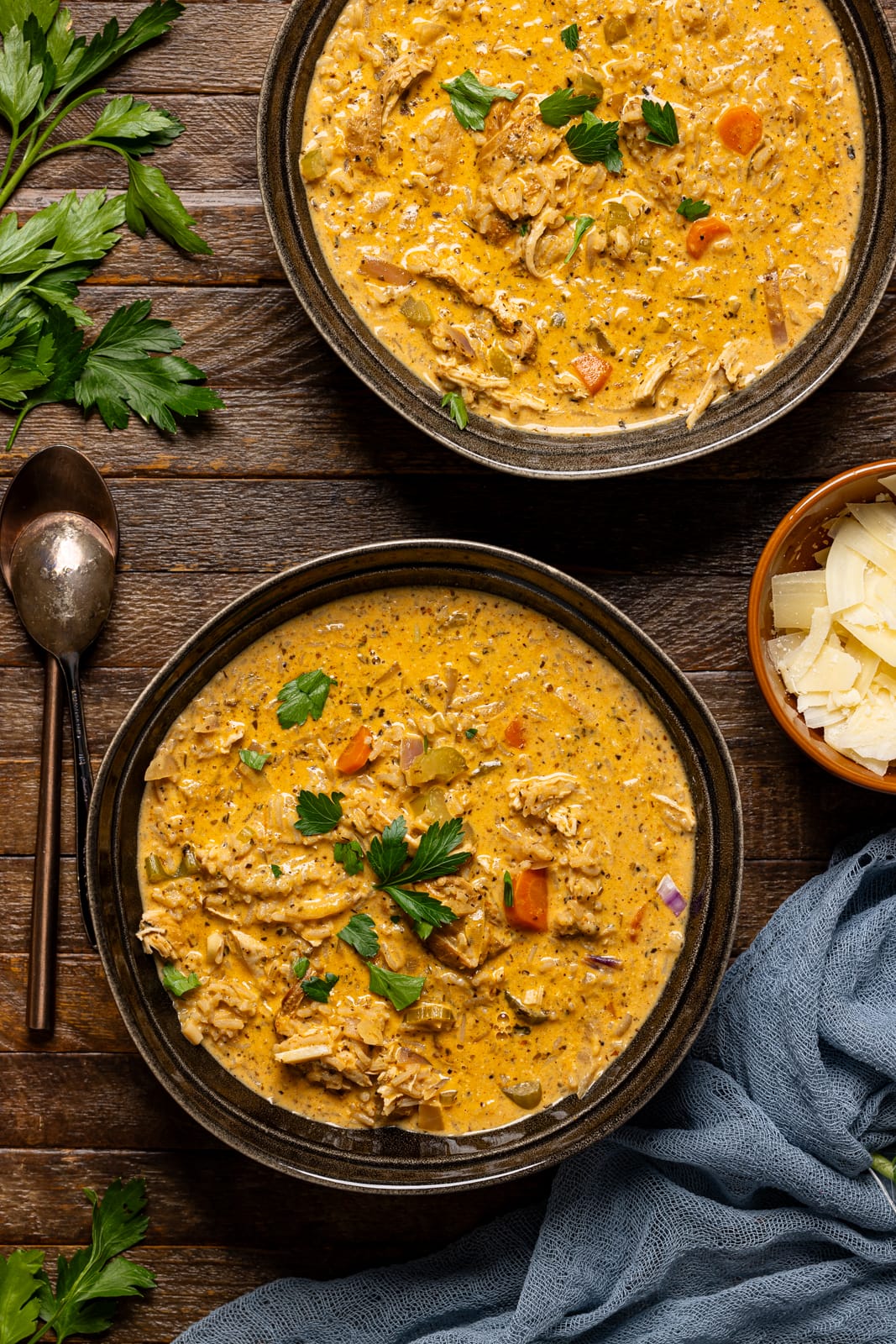 Two bowls of soup with spoons and parmesan cheese.