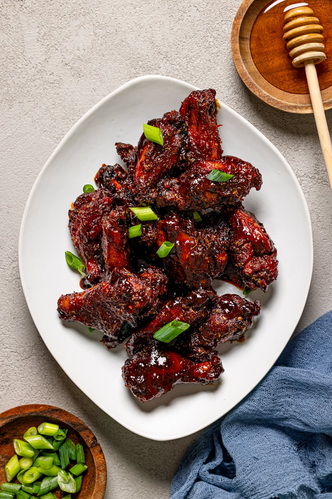 Honey BBQ wings on a white plate with a side of honey and green onions.