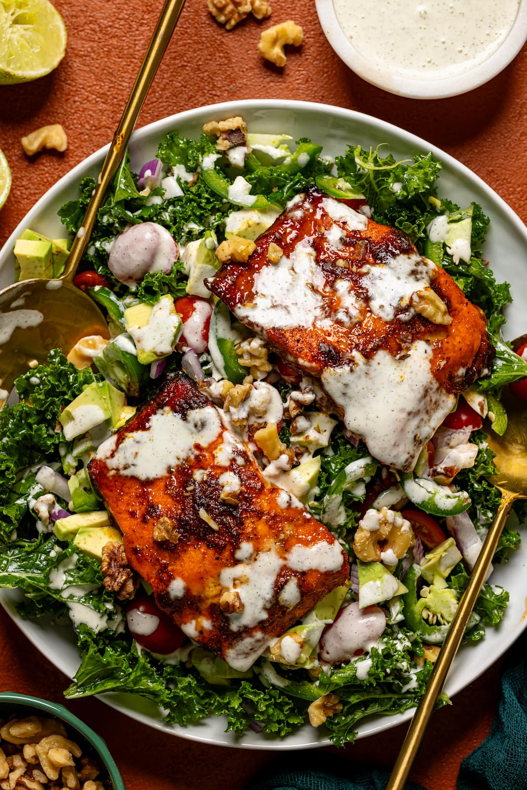 Salad in a platter with two serving utensils and dressing.