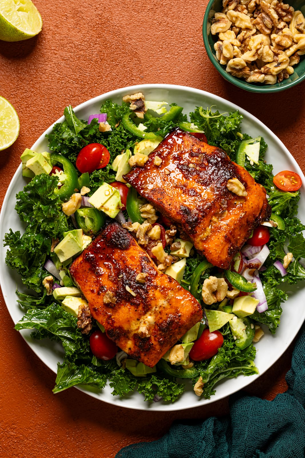 Glazed salmon atop salad in a platter with walnuts and lime.