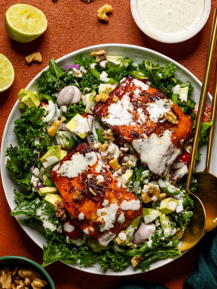 Salad in a platter with two serving utensils and dressing.