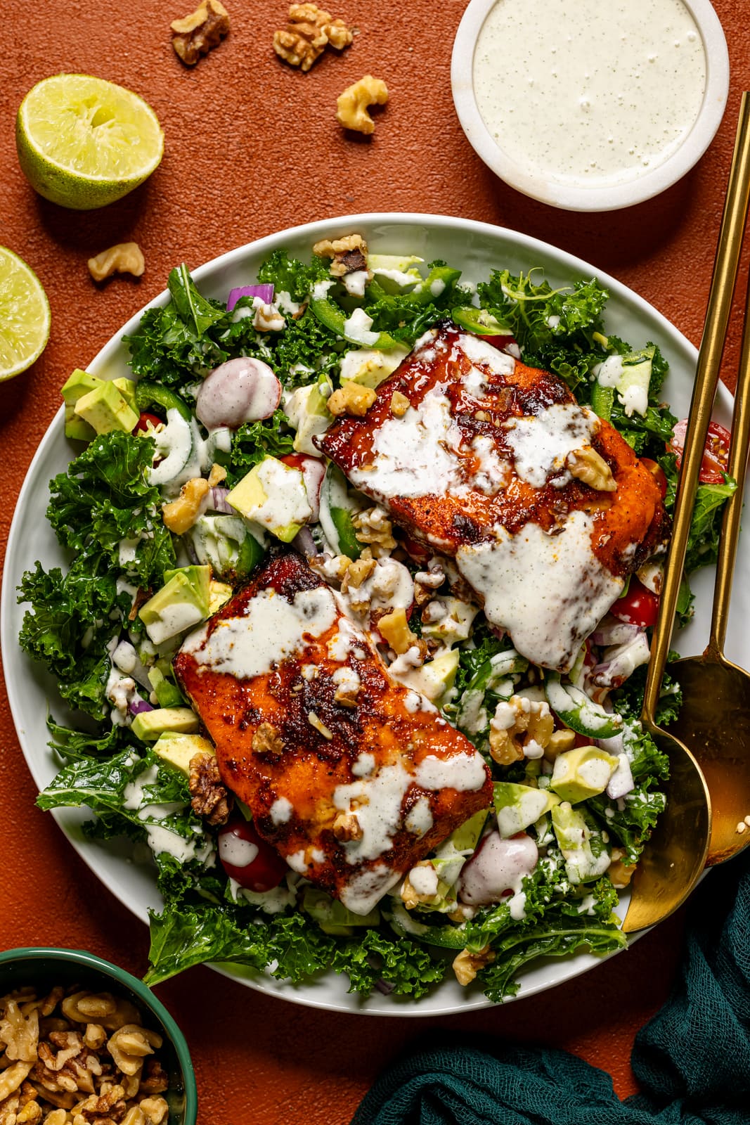 Salad in a platter with two serving utensils and dressing.