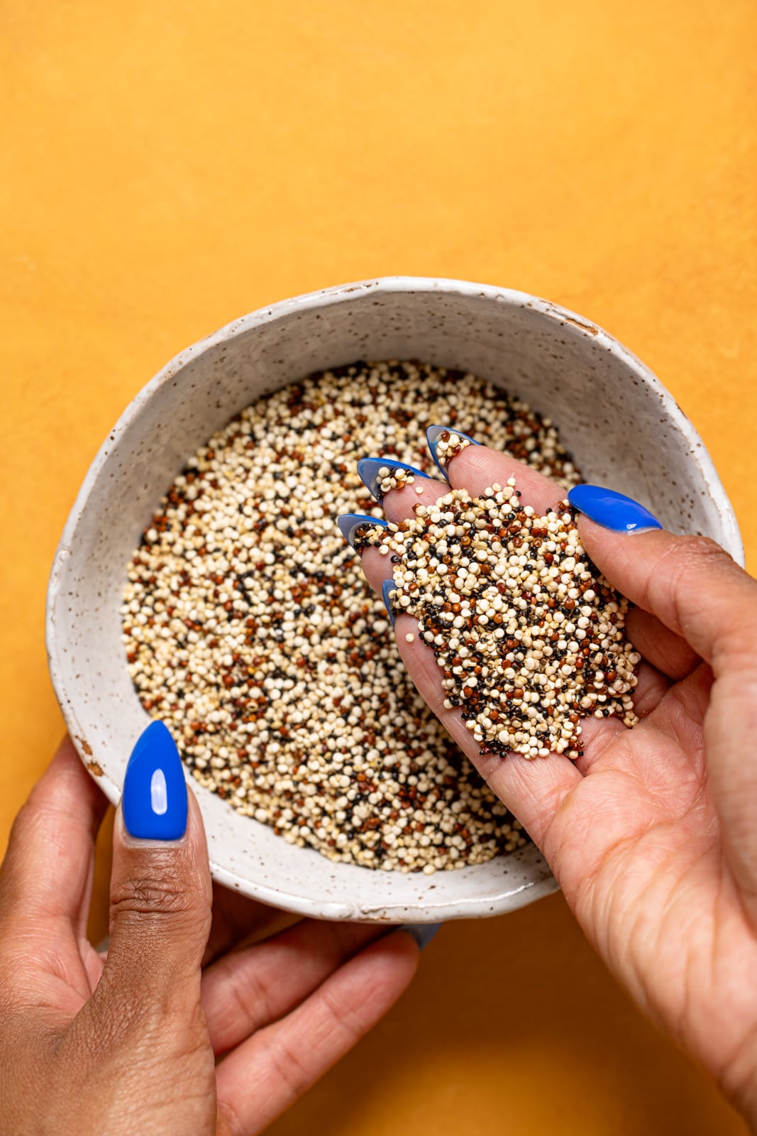 A bowl with dry quinoa being held with hands.
