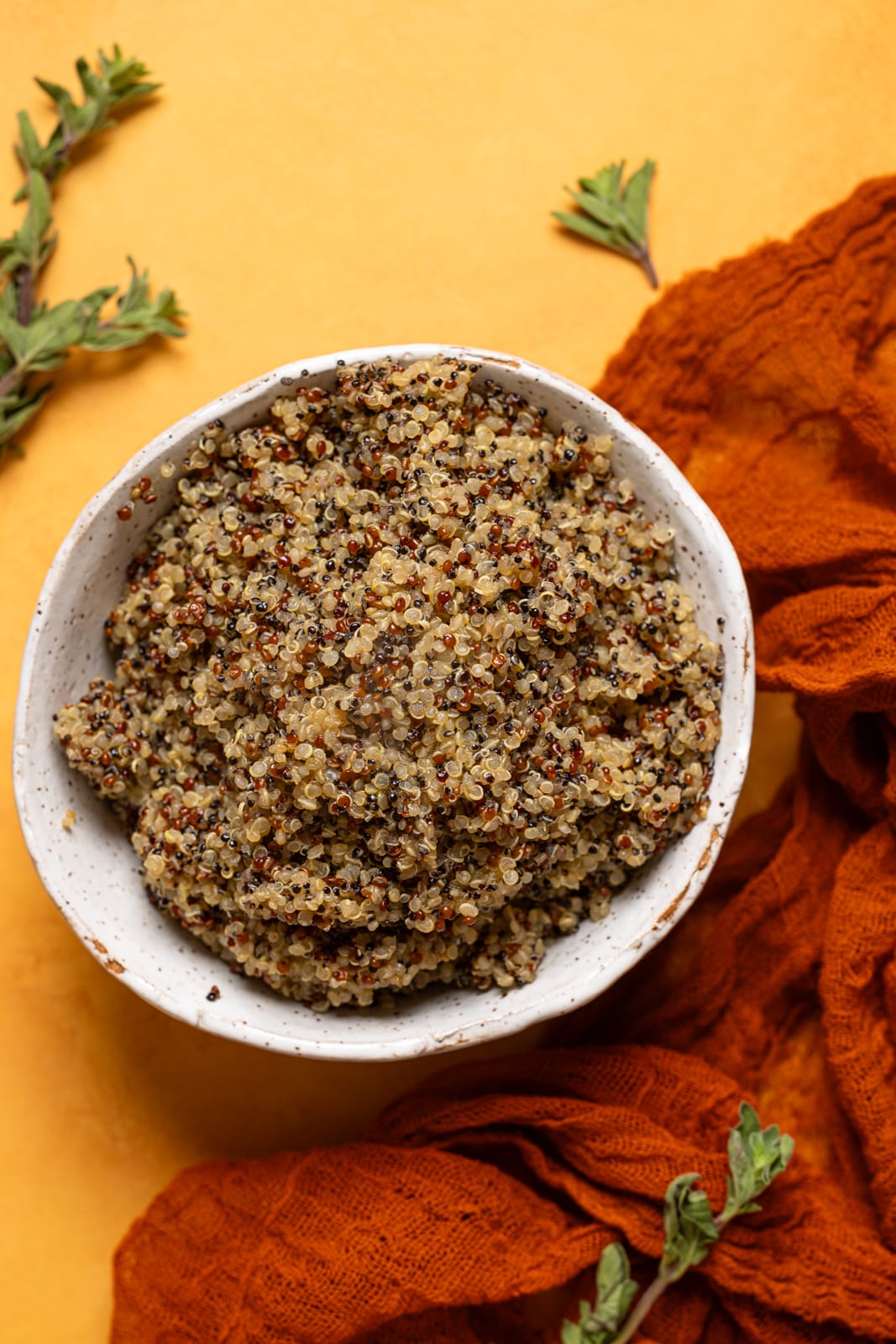 A bowl of quinoa on an orange table with a red napkin.