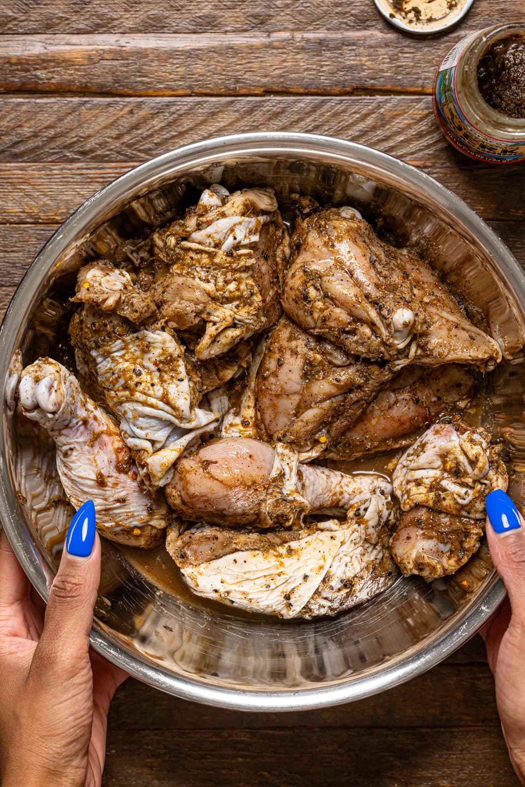 Marinated chicken in a silver bowl being held.