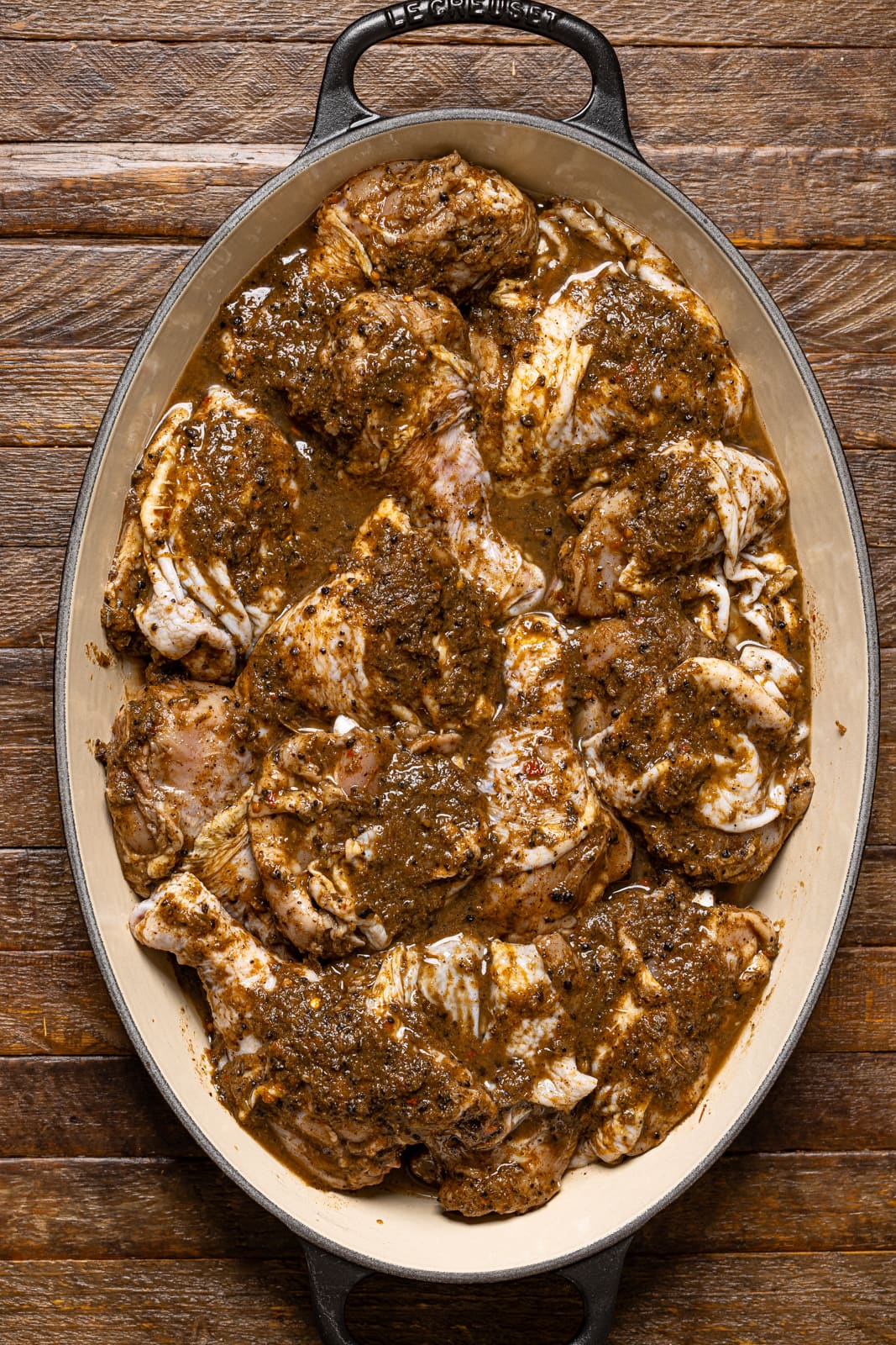 Marinated chicken lined in a baking dish on a brown wood table.