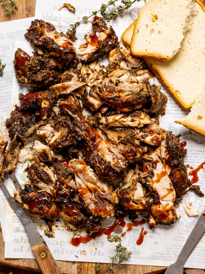 Chopped jerk chicken on a cutting board with BBQ sauce, bread, and a fork.