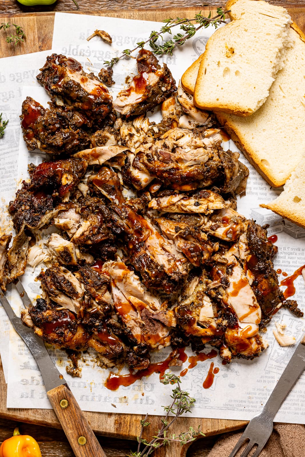 Chopped jerk chicken on a cutting board with BBQ sauce, bread, and a fork.