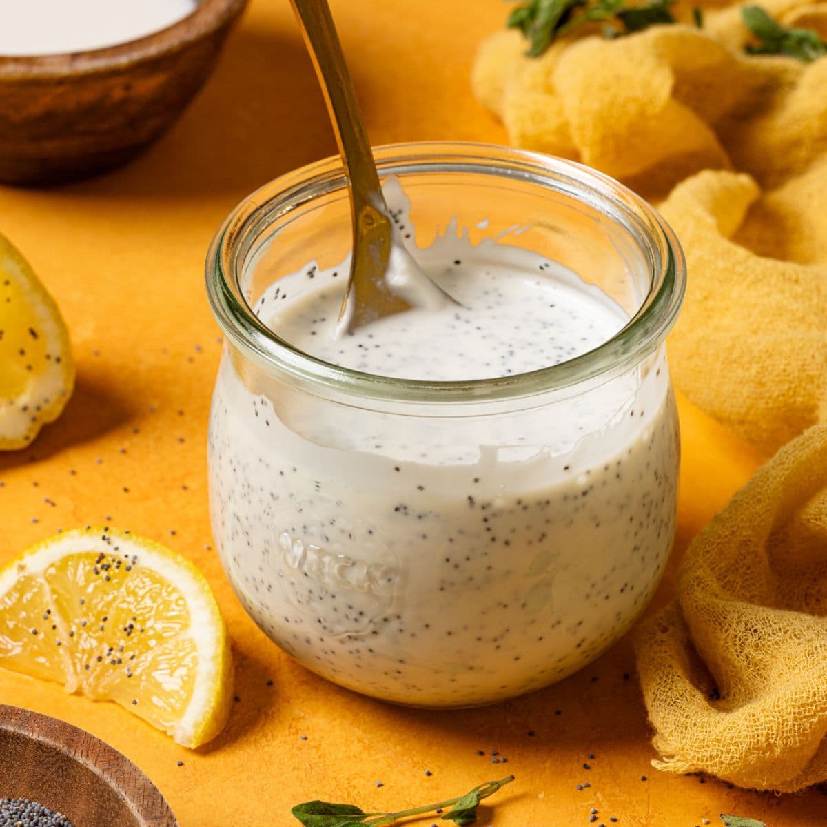 Lemon poppyseed dressing in a mason jar with a spoon and lemon wedges.