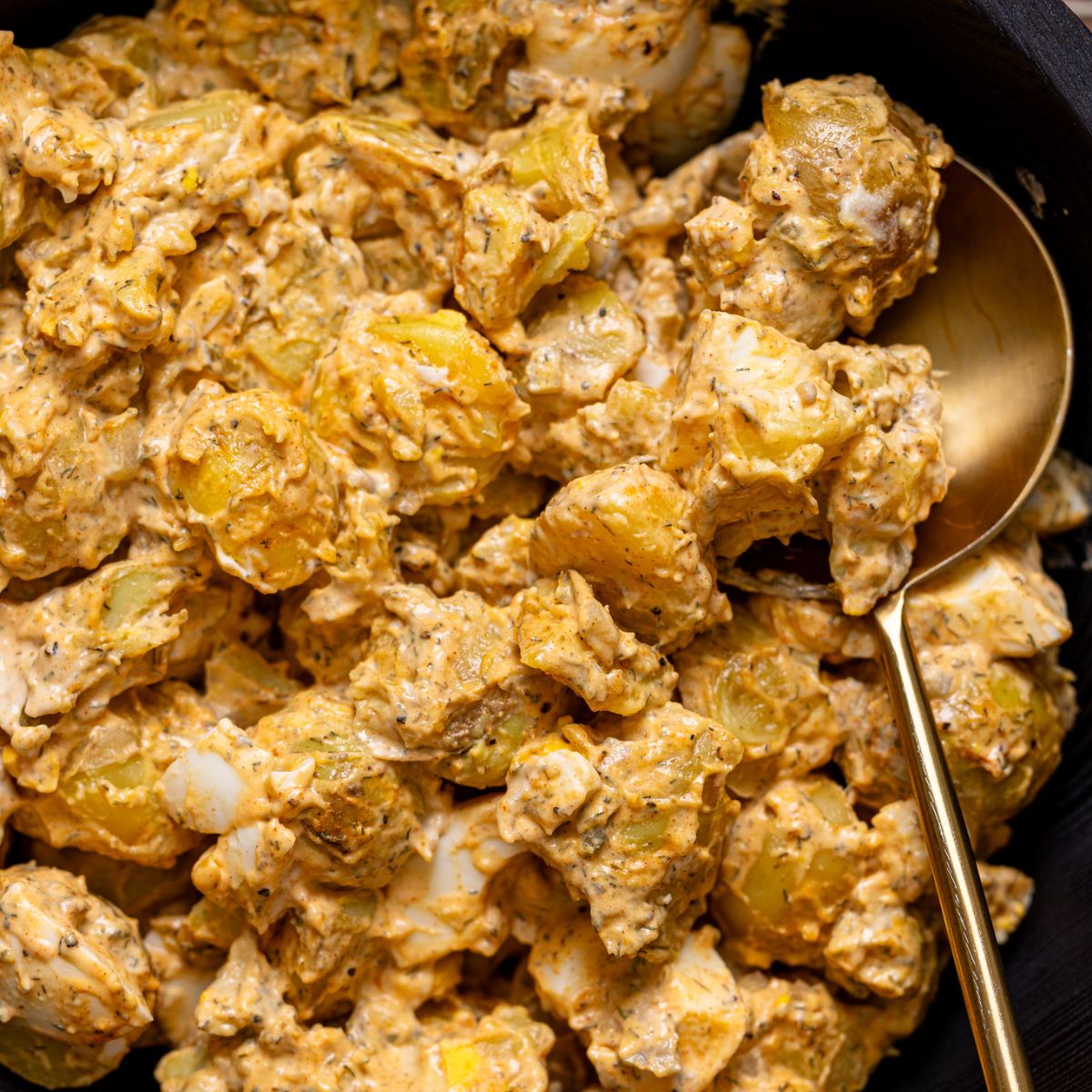 Up close shot of potato salad in a black bowl with a spoon.