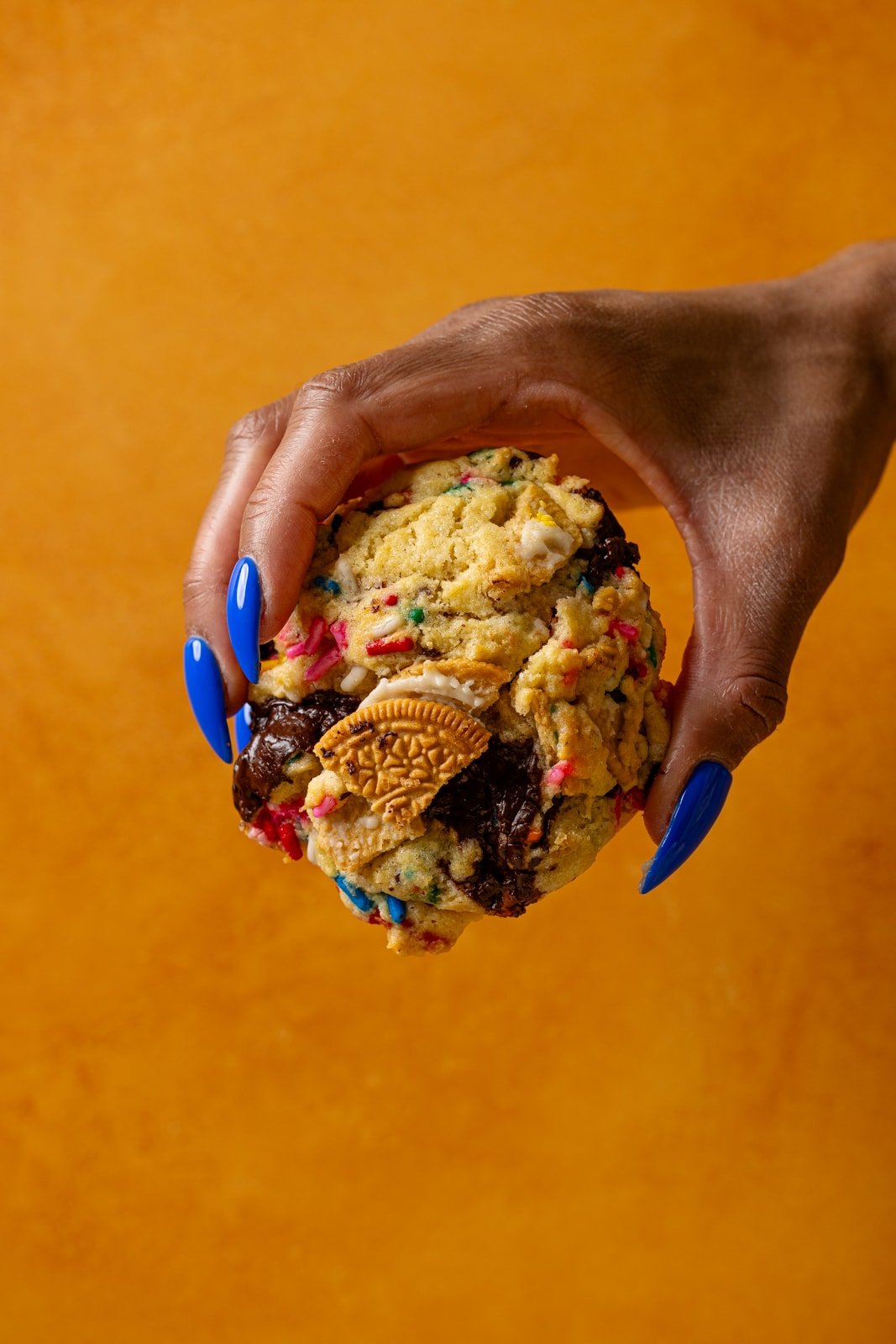 Cookie being held with hand in front of an orange background.