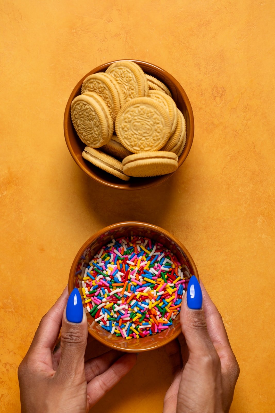 Bowls of Oreos and sprinkles on an orange table.