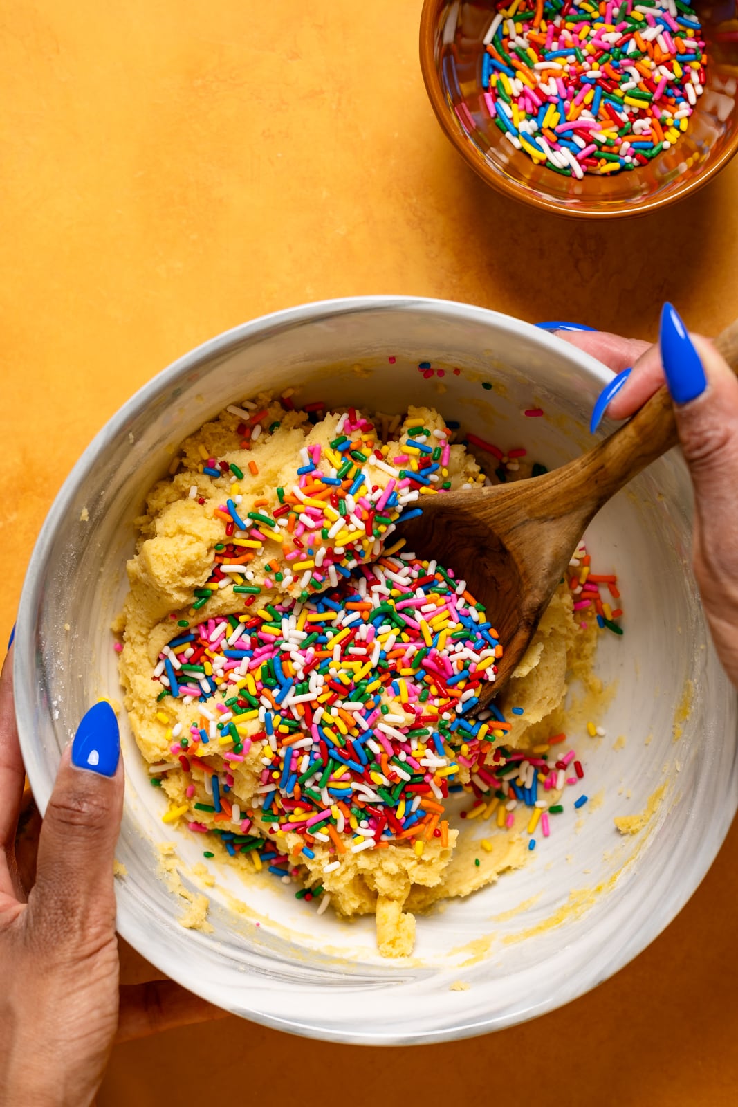 Cookie batter with sprinkles in a bowl with a wooden spoon.