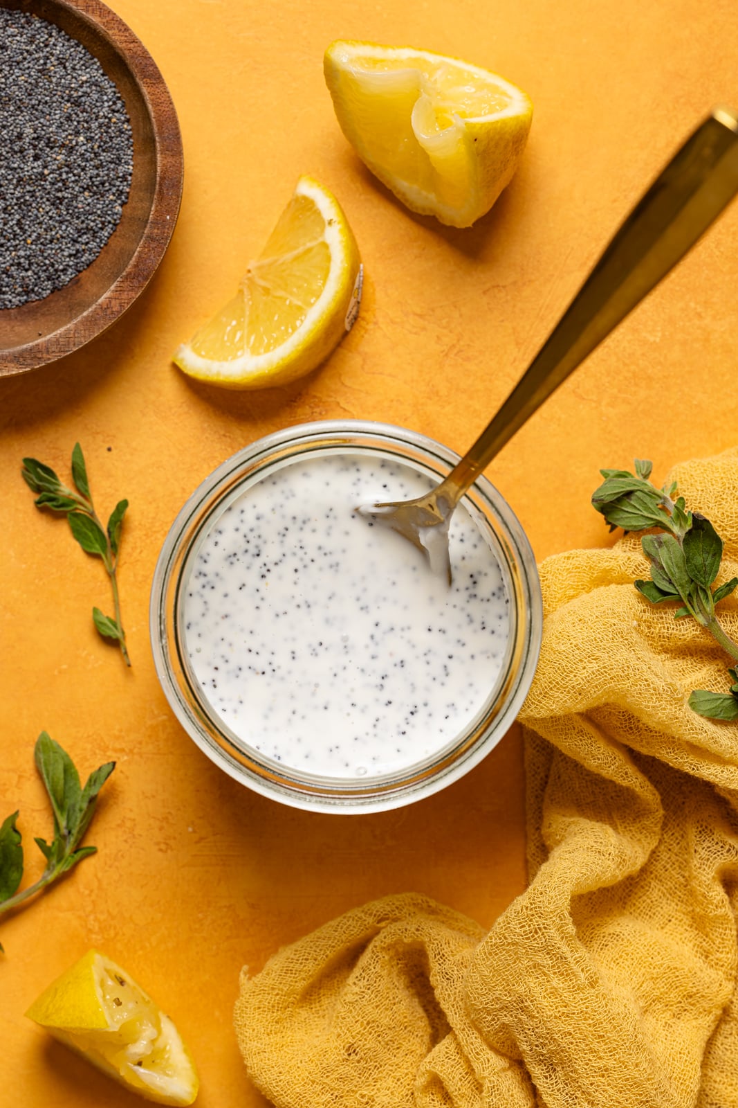 Dressing in a mason jar on an orange table with lemons and poppyseeds.