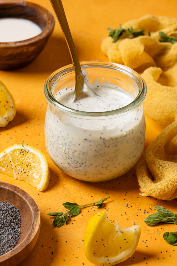 Lemon poppyseed dressing in a mason jar with a spoon and lemon wedges.